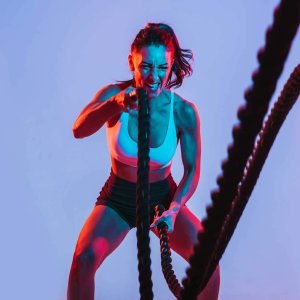 woman with fierce face exercising with heavy ropes. neon lights shining on her