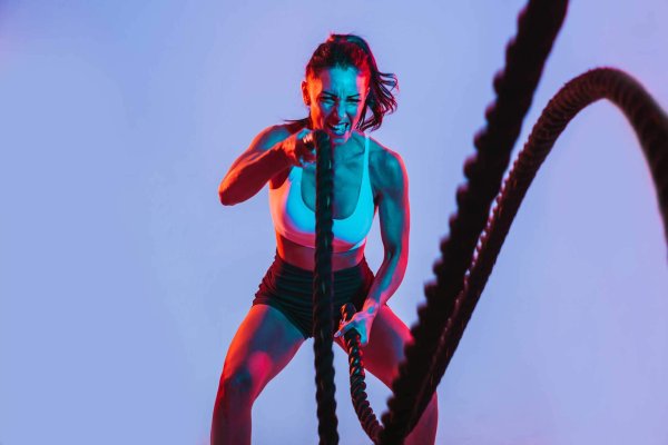 woman with fierce face exercising with heavy ropes. neon lights shining on her