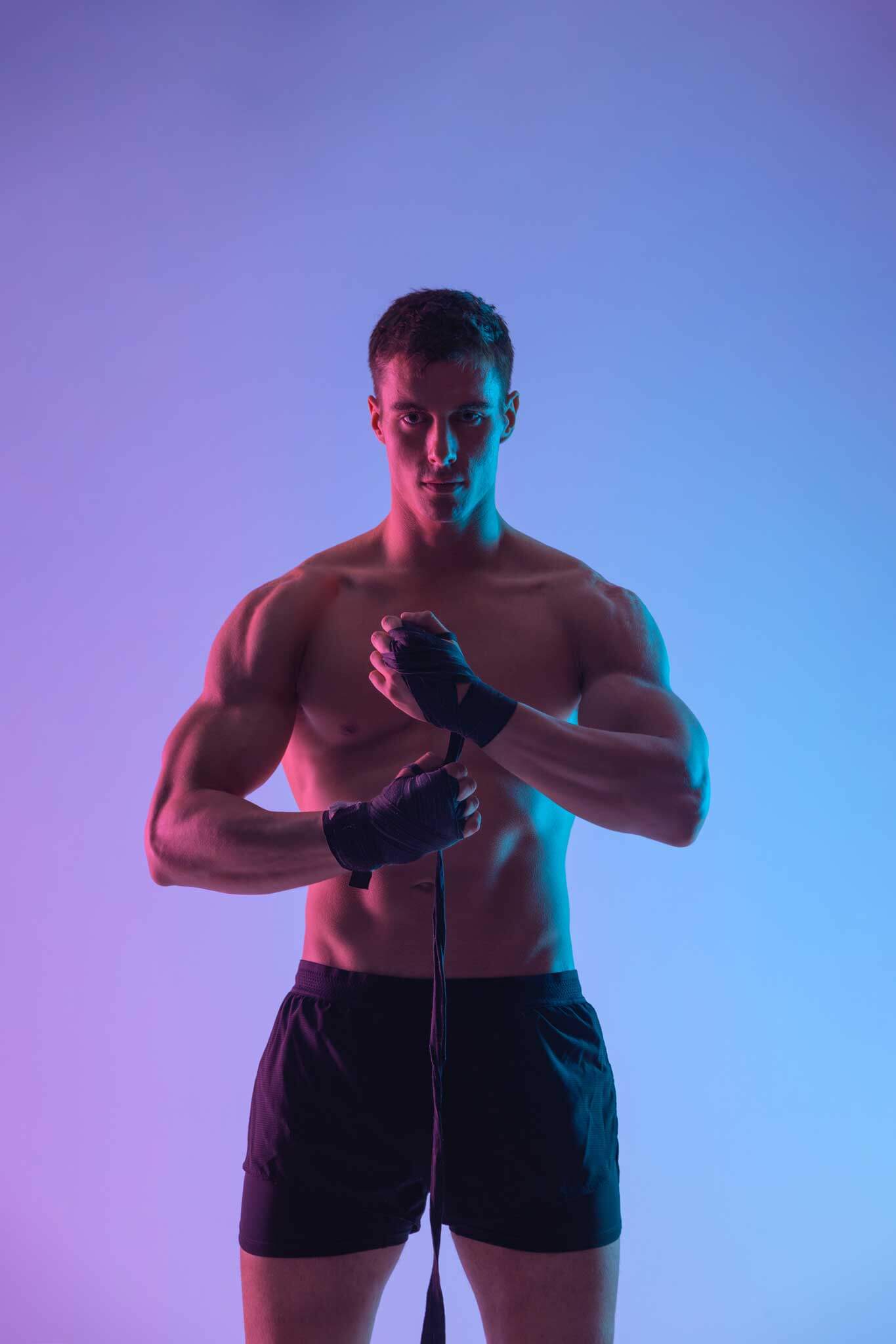 male putting on hand straps to lift weights against blue and purple neon background